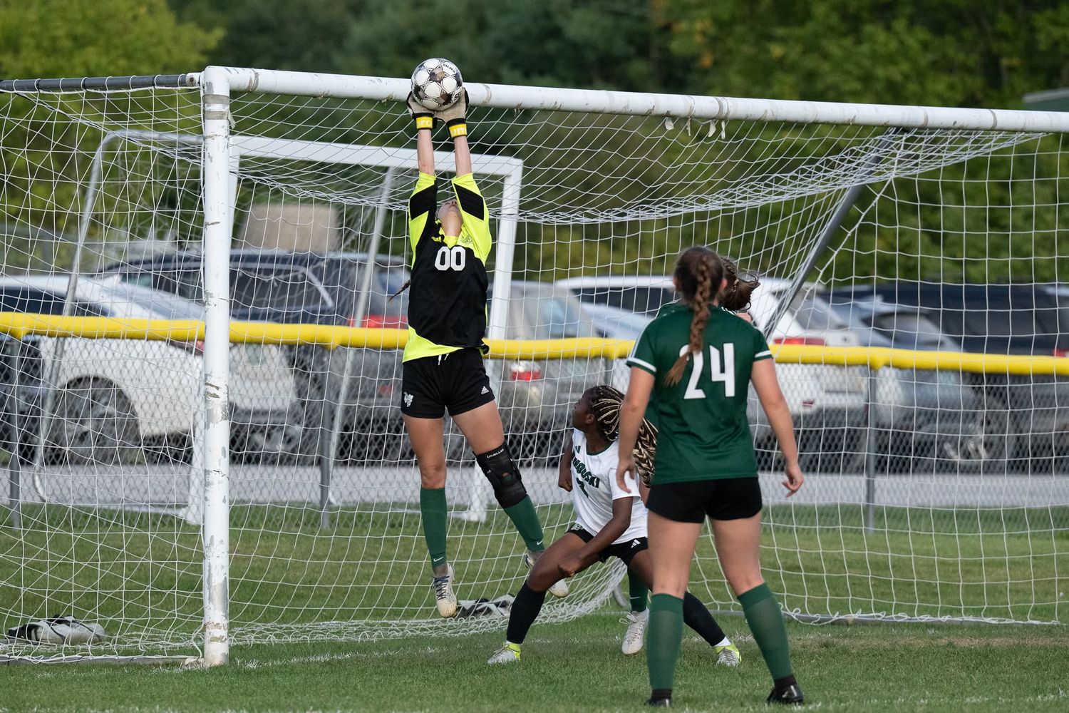 Female goalkeeper in yellow jersey leaps to catch soccer ball above the net during a girls school match.
