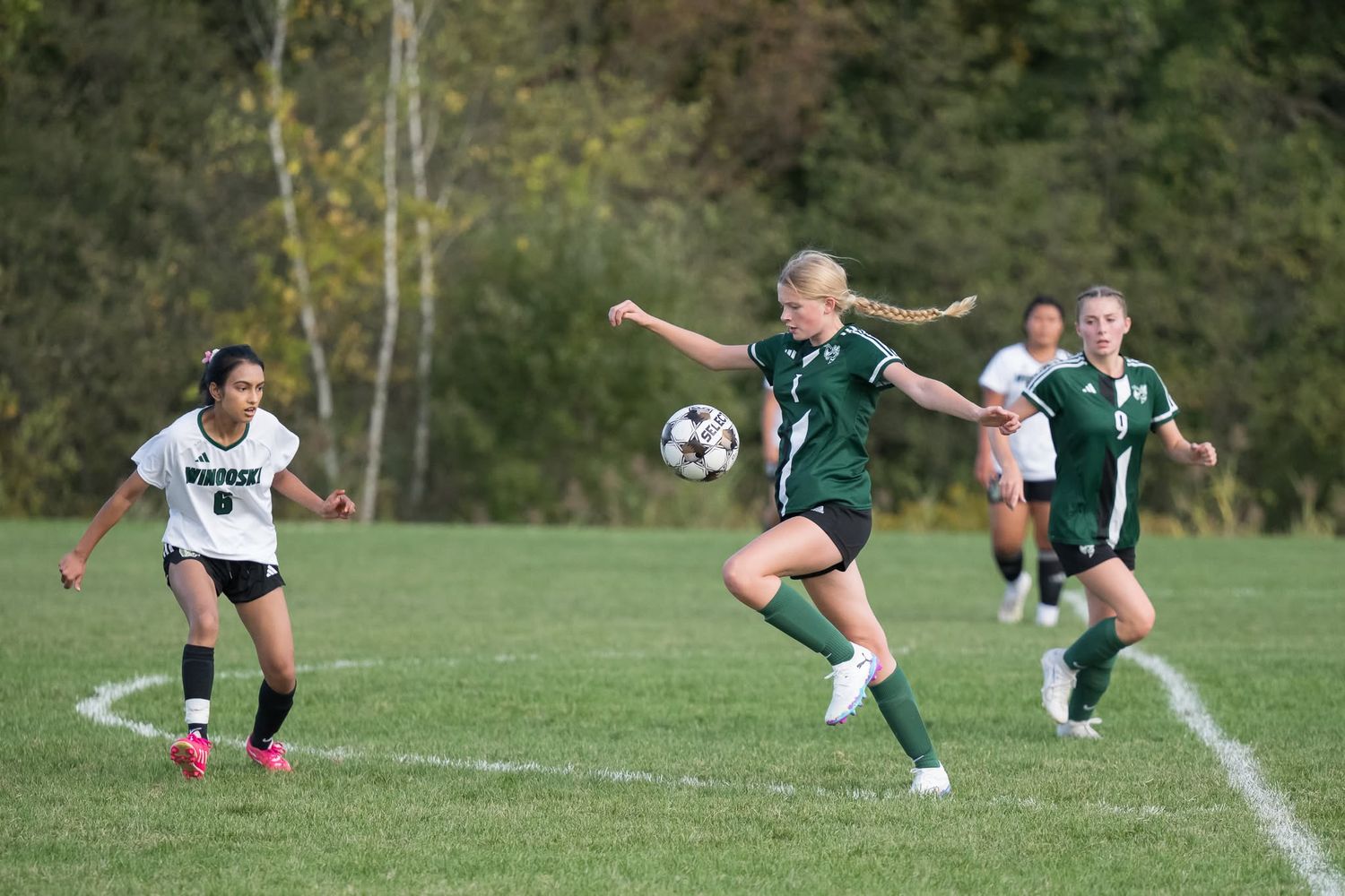 Female soccer player in green uniform controls the ball during a competitive girls school soccer game.