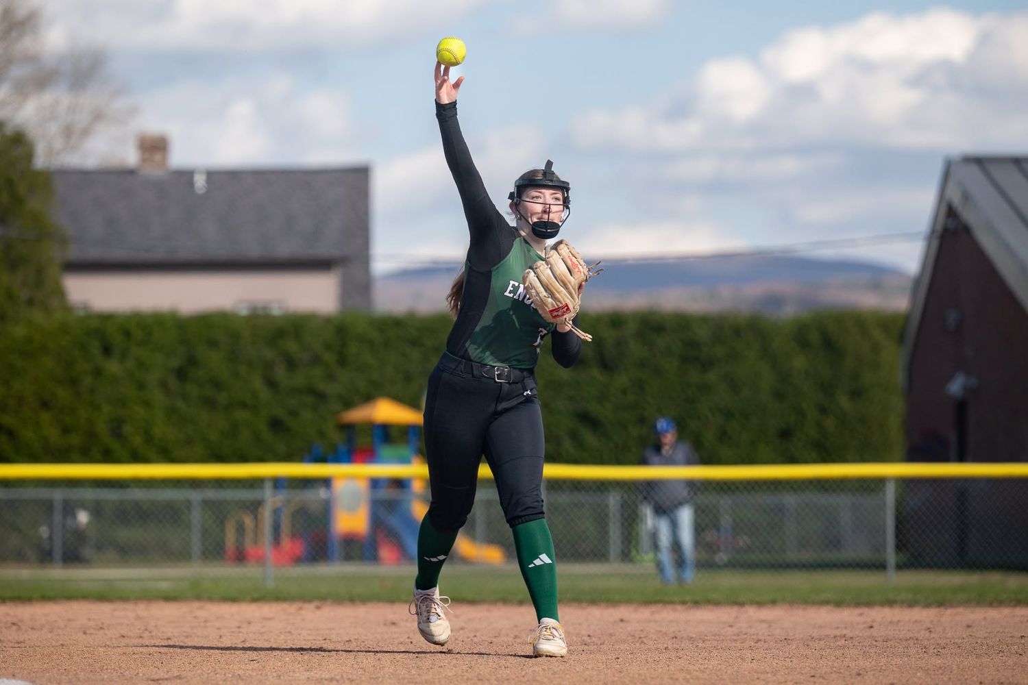Northern Vermont softball player winds up to throw yellow ball during a school game.