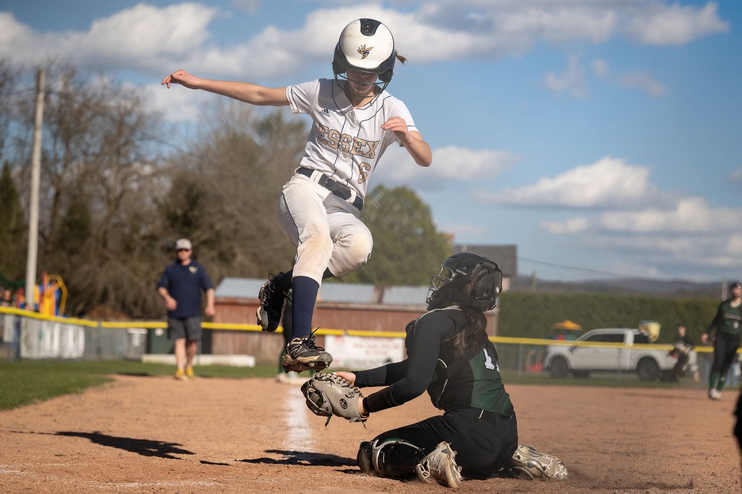 Essex Vermont softball player leaps over sliding fielder at base during a competitive high school girls softball game.