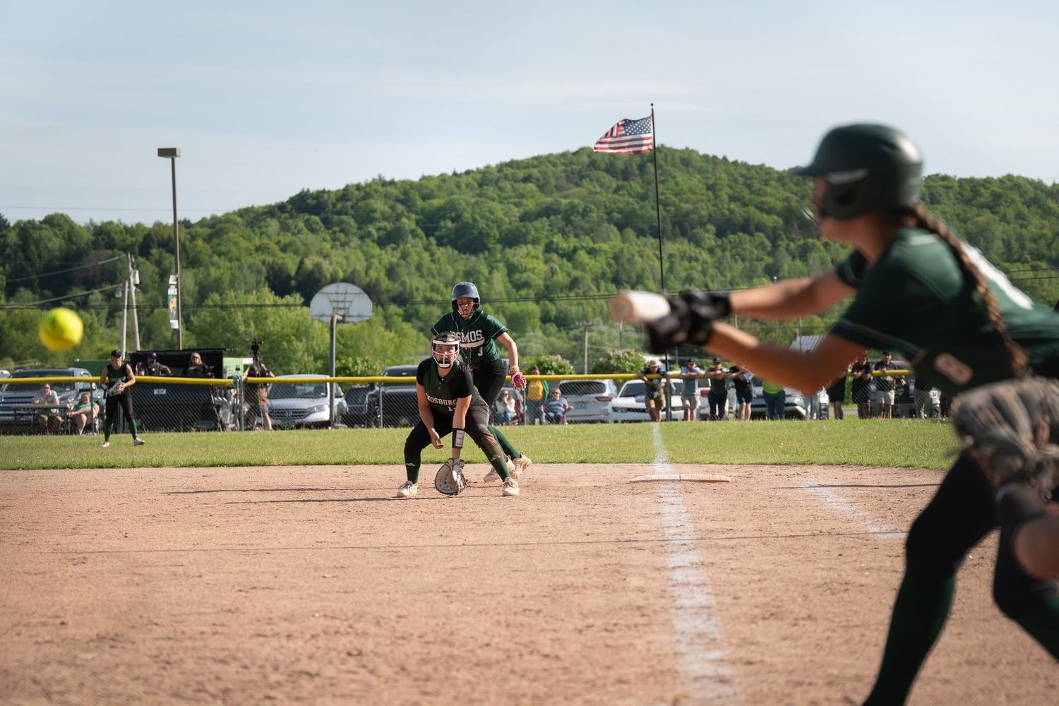 Vermont softball batter prepares to swing as pitcher delivers yellow ball during a high school game.