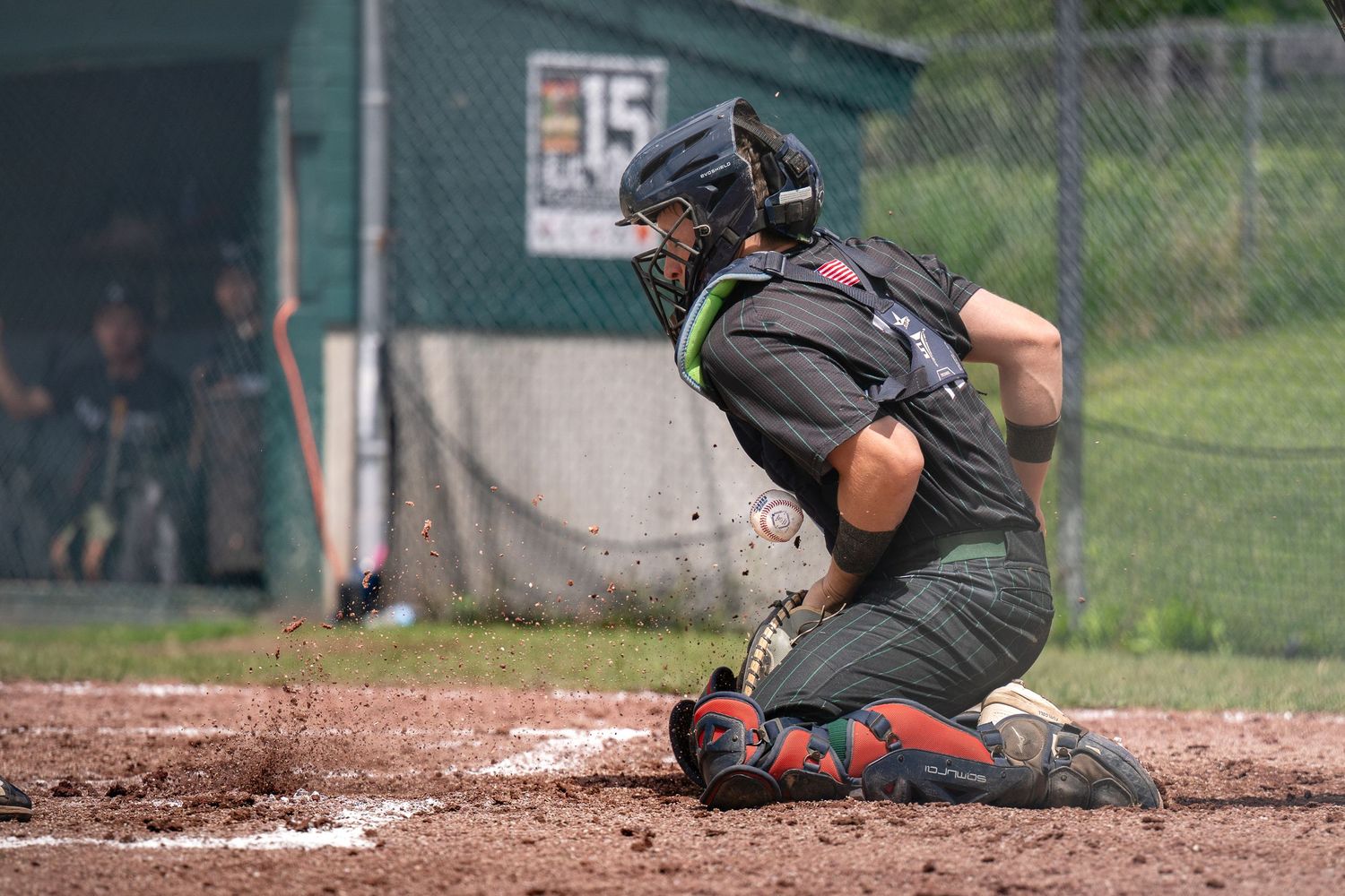 Baseball catcher in dark uniform crouches at home plate during a game.
