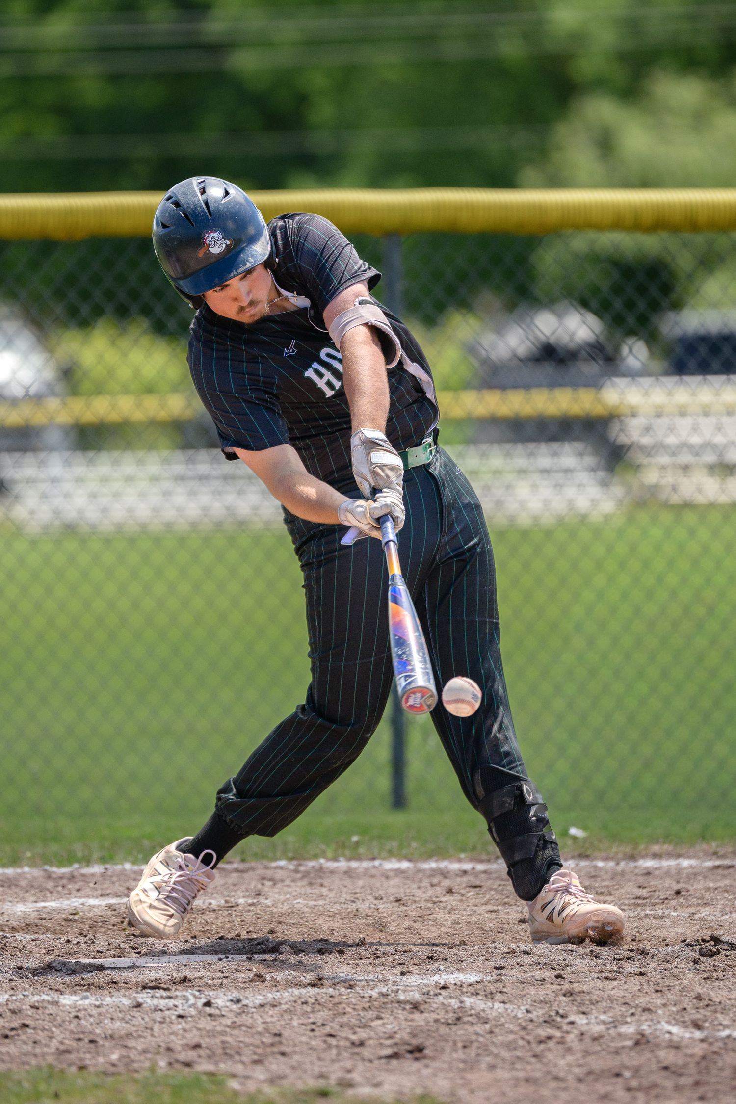 Vermont High school baseball batter in black pinstripe uniform makes contact with ball during an Enosburg High School game.