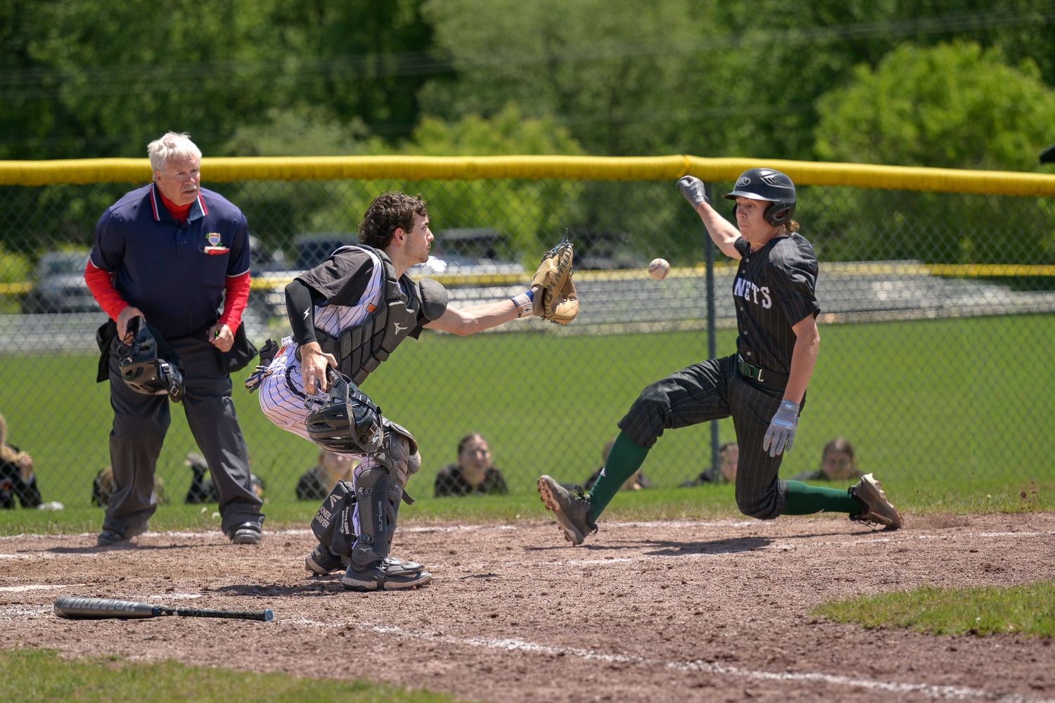 Baseball catcher tags out a sliding player at home plate as umpire watches closely.