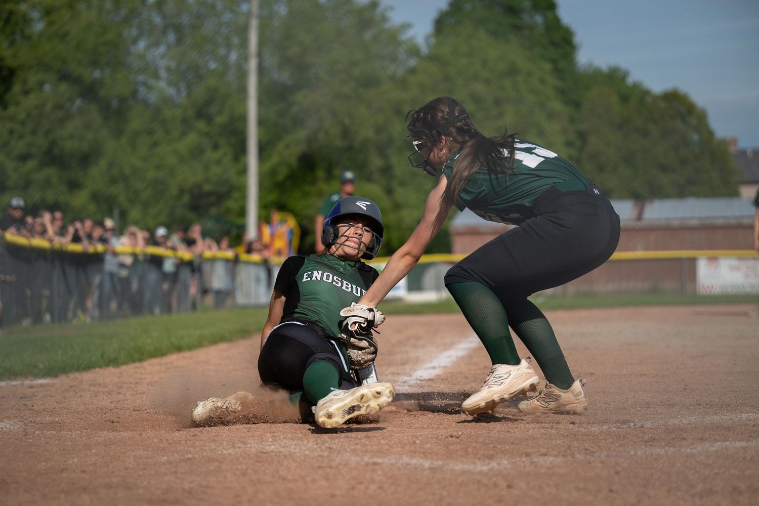 Softball player slides into base as fielder in green uniform applies the tag.