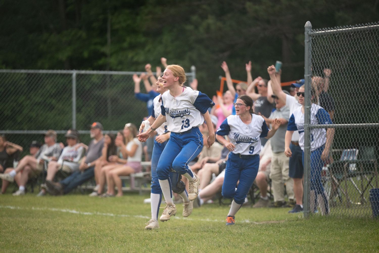 Softball player in blue uniform runs bases as crowd cheers in the background.