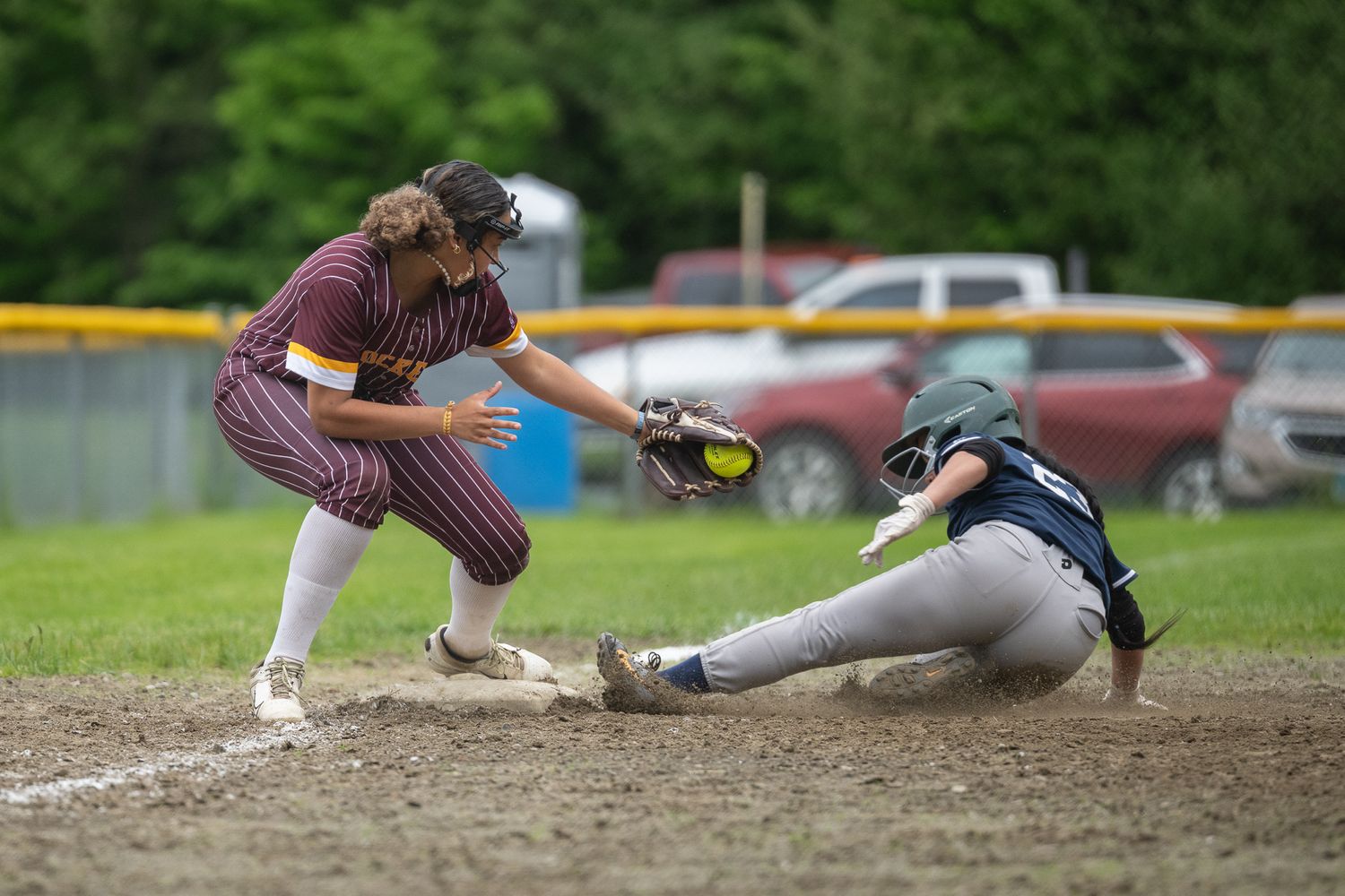 Softball player slides into base as fielder attempts tag with ball in glove during youth game.