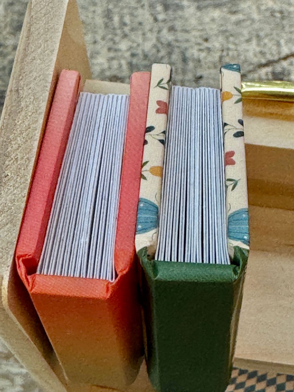 Three small handmade hardcover miniature books with colorful spines in red, floral, and green standing upright.
