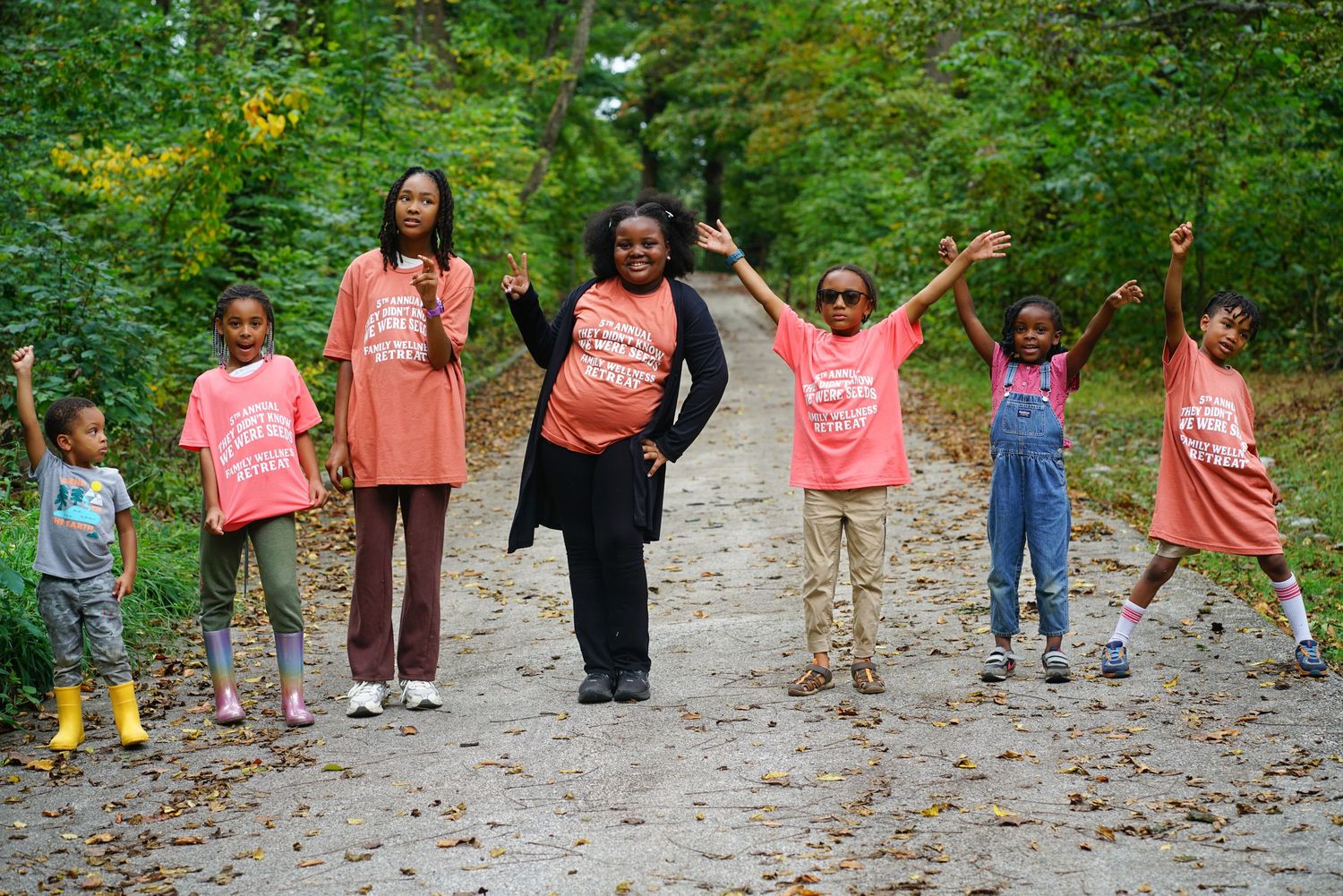Group of children and adults in matching pink shirts posing on a forest path surrounded by green trees.