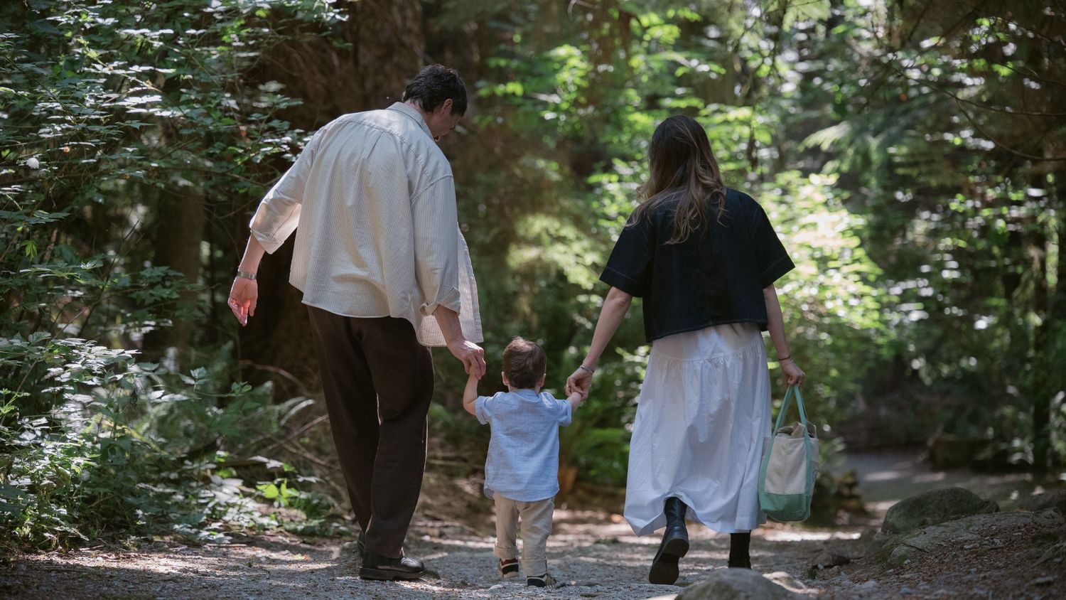 A young family of 3 walking hand-in-hand down a forest trail at Lighthouse Park, West Vancouver candid family photography by Tashtakespics