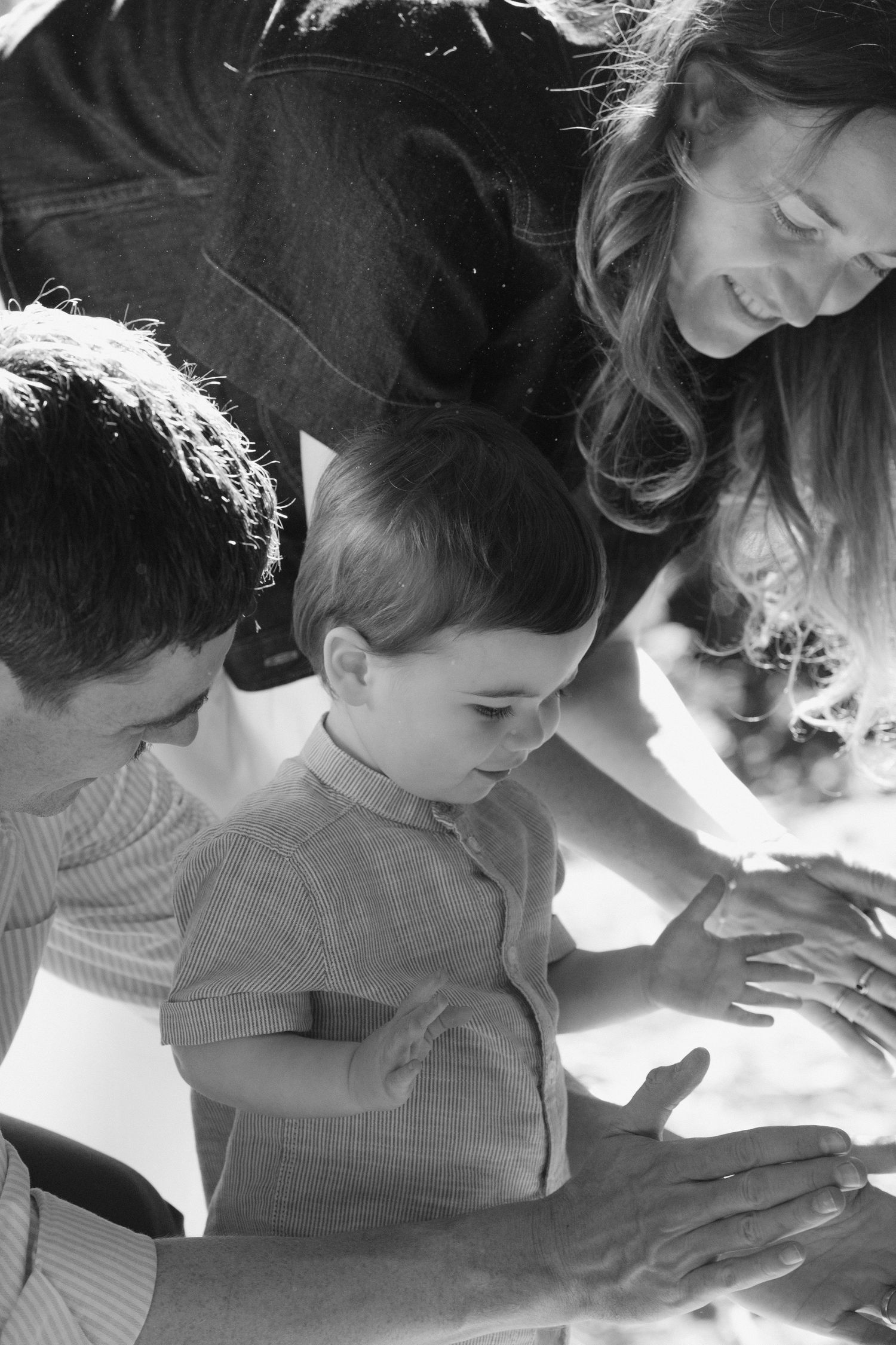 Black white overhead photo of parents leaning in with their young child all 3 focused on something, family photography by Tash Takes Pics