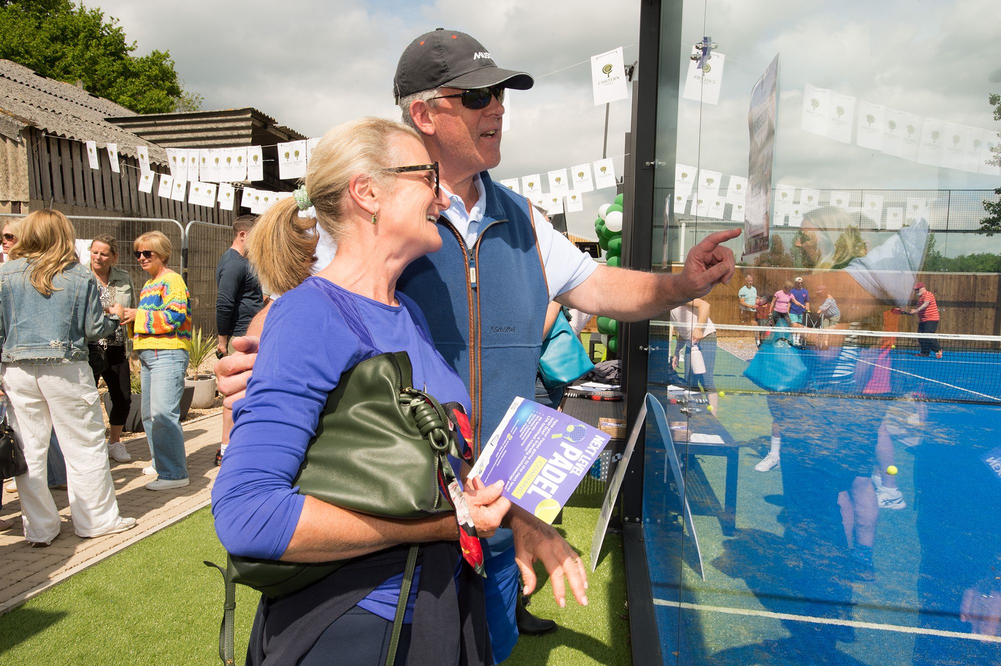 A man and woman stand side by side in front of a glass wall during the Chiltern Padel launch party in Buckinghamshire.