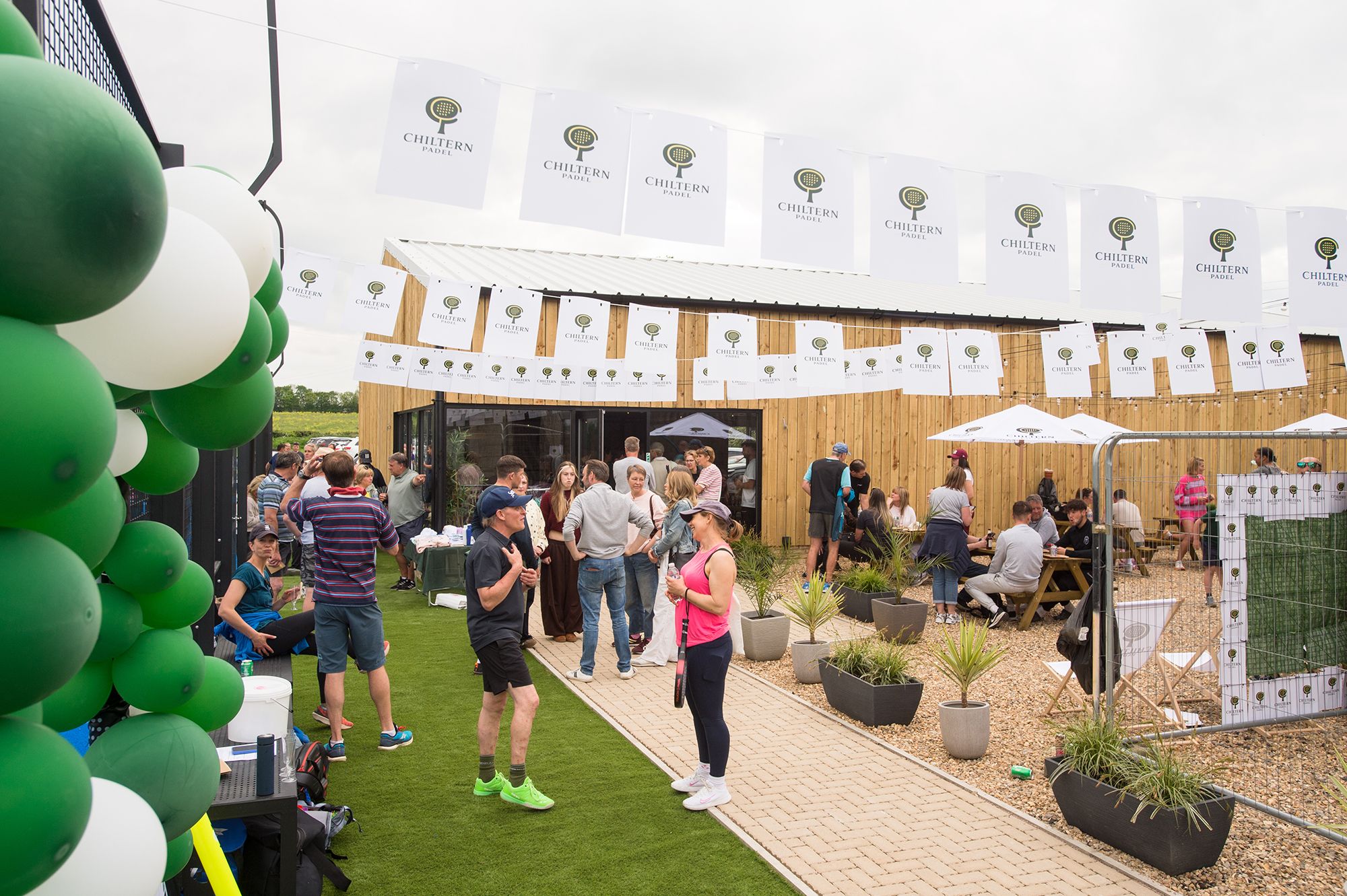 Attendees stand around a green and white flags at the Chiltern Padel launch party in Buckinghamshire, captured by Abigail's studio.