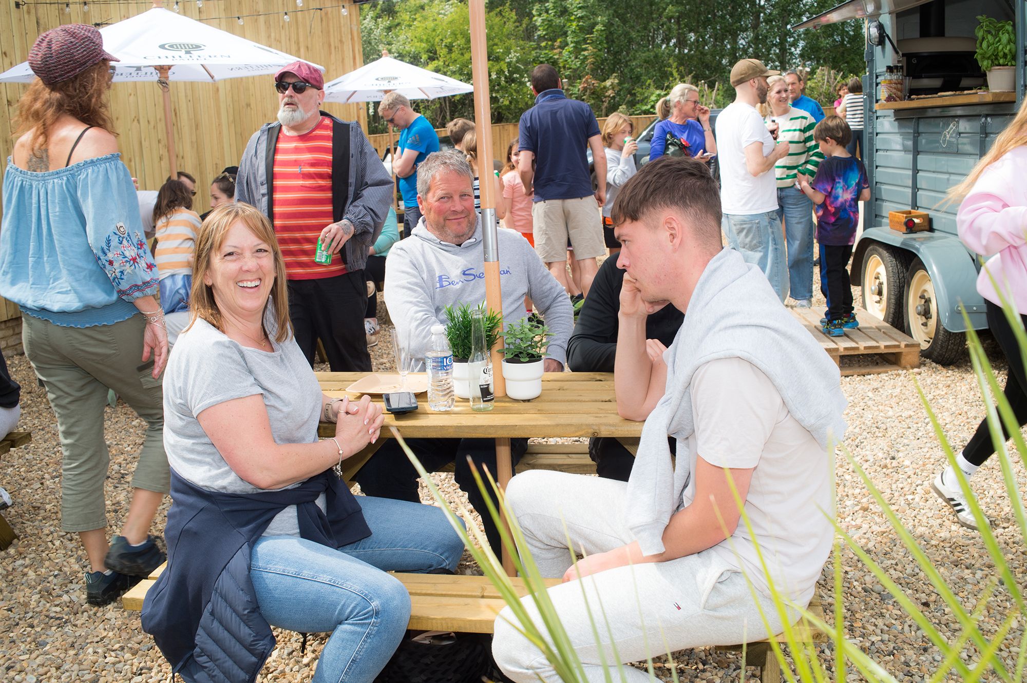 A group of people enjoying a picnic at a table during the Chiltern Padel launch party, captured by Abigail's studio.