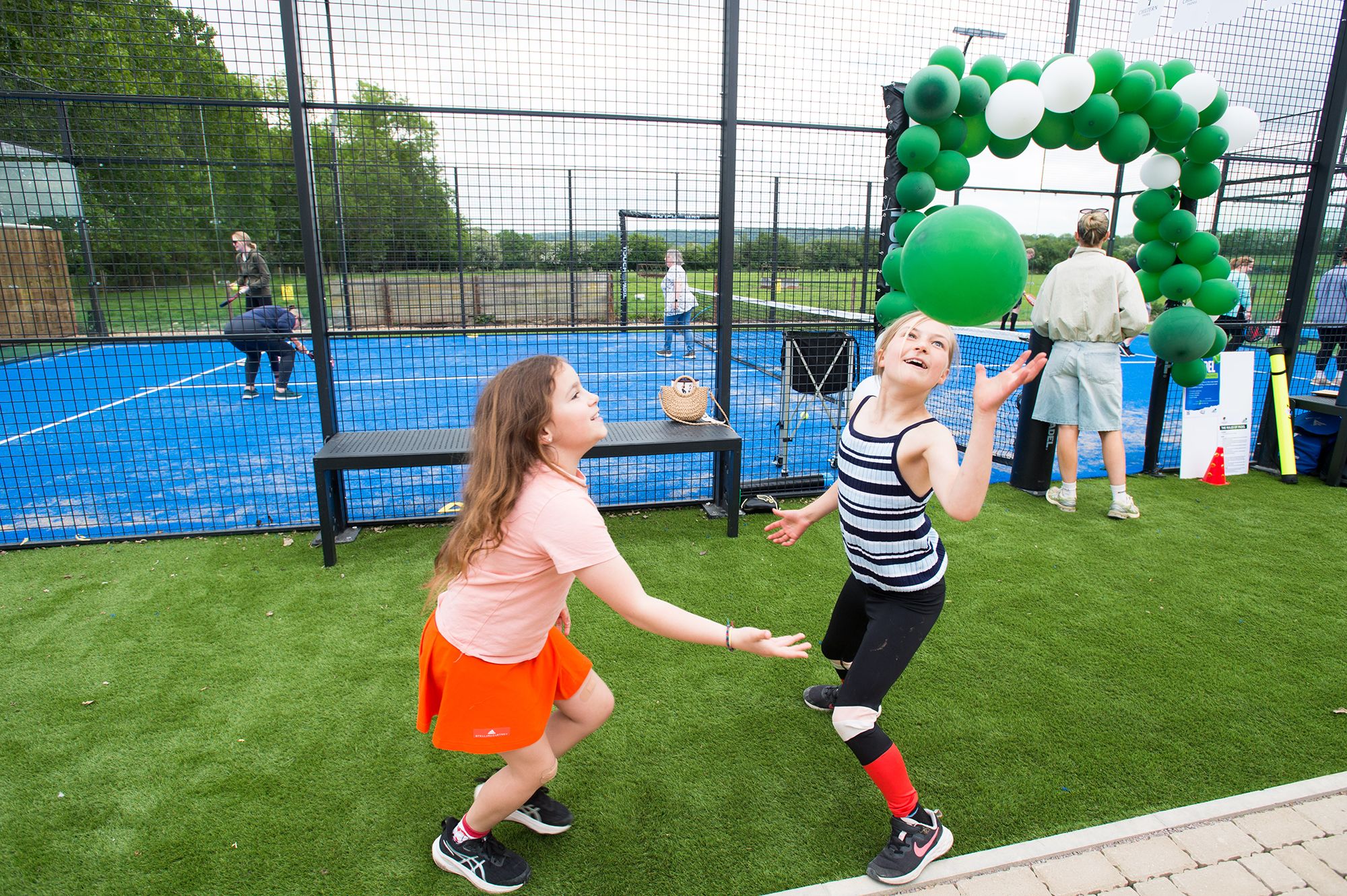 Two girls engaged in a balloon tennis match on artificial grass at the Chiltern Padel launch party, photographed by Abigail's studio.