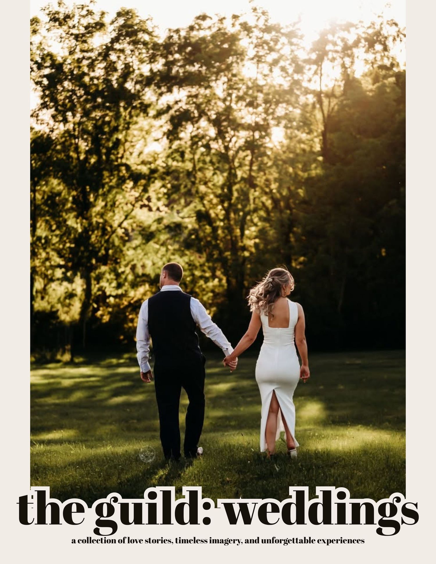 A bride and groom walk hand in hand through a sunlit green meadow surrounded by trees on their wedding day.