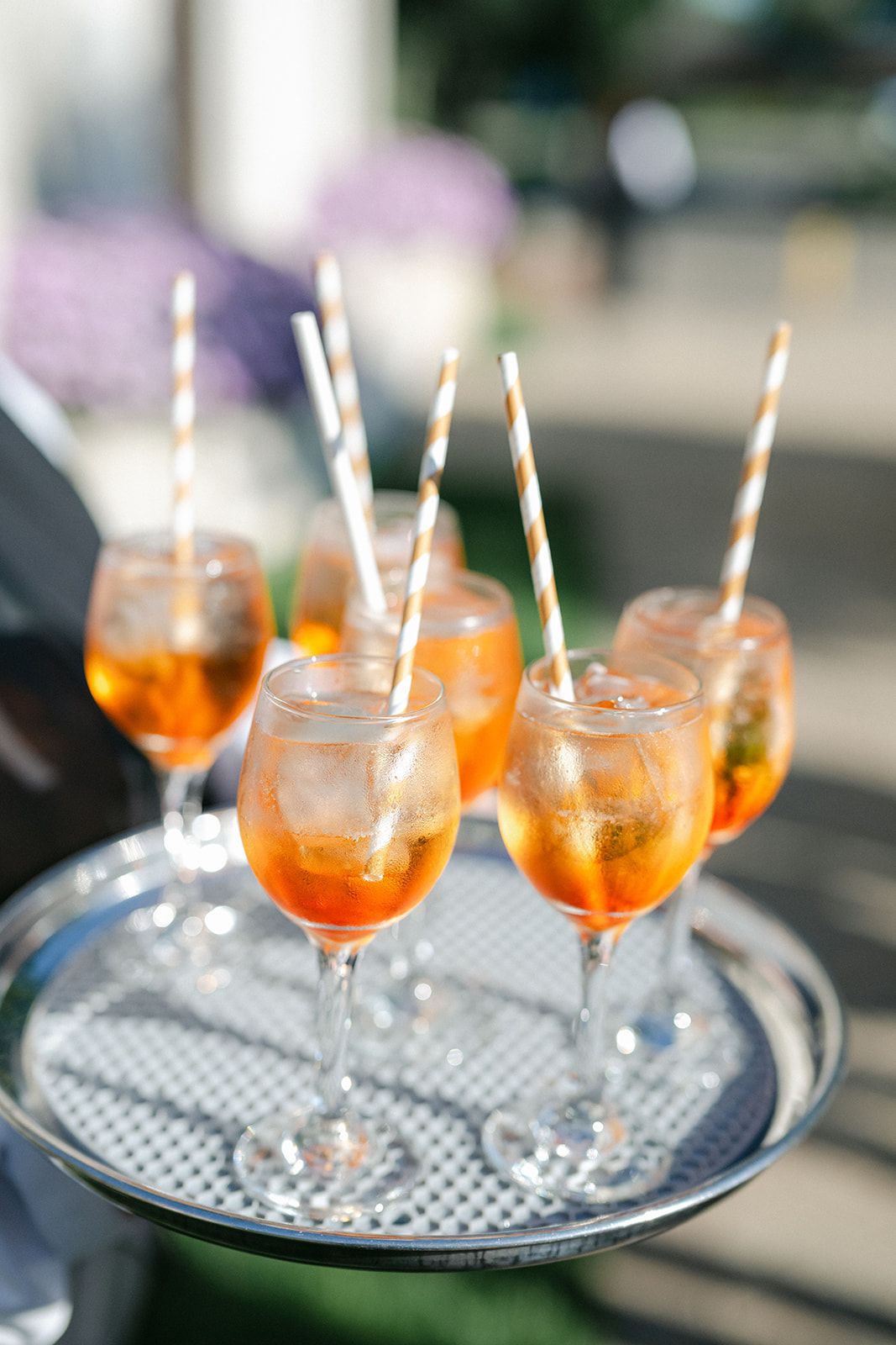 Armour House Wedding - Silver tray with orange Aperol Spritz cocktails in wine glasses with striped paper straws served outdoors.