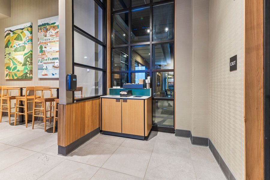 Modern Starbucks interior with wooden service counter, large windows, tile flooring, and colorful wall art near dining area.