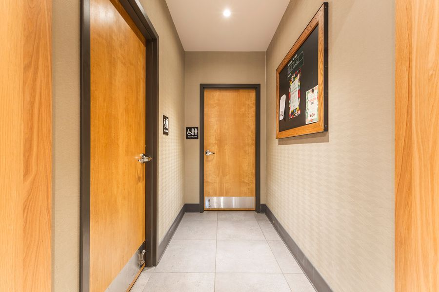 Narrow hallway with warm wood doors, tile flooring, and framed artwork on beige textured walls.