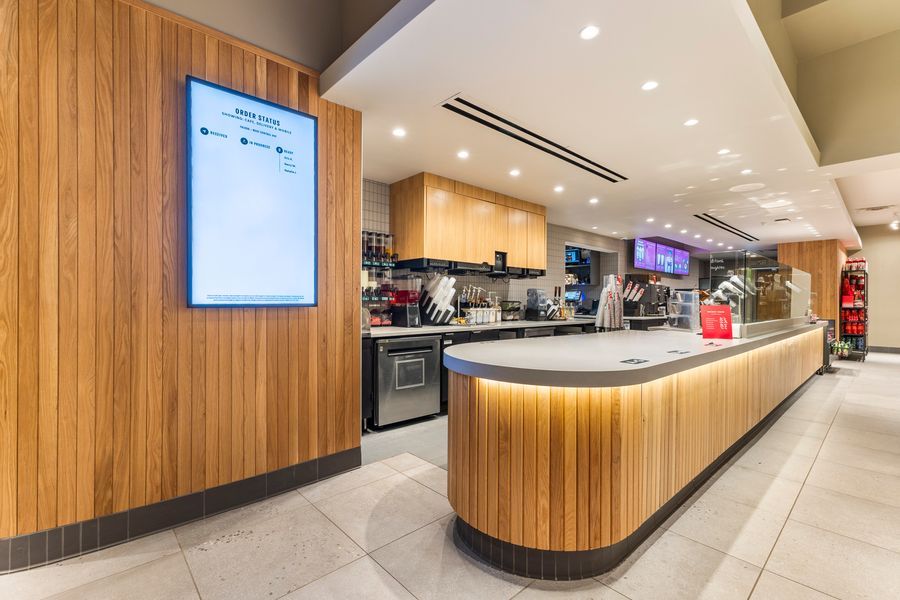 Modern cafe counter with wooden paneling, digital menu board, and sleek curved service desk in a bright interior.
