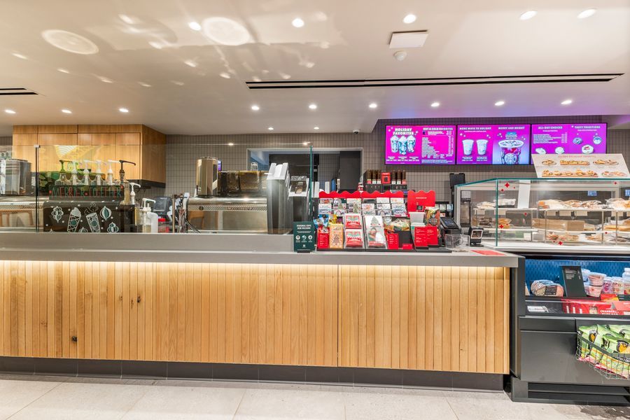 Modern cafe counter with wooden paneling, digital menu boards, and display cases in a bright commercial space.