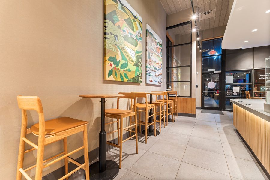 Cozy cafe seating area with wooden bar stools, high tables, and colorful botanical wall art.