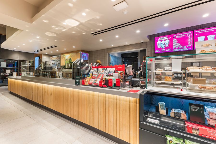 Modern fast food counter with wooden paneling, digital menu boards, and a well-lit display case in a contemporary restaurant.