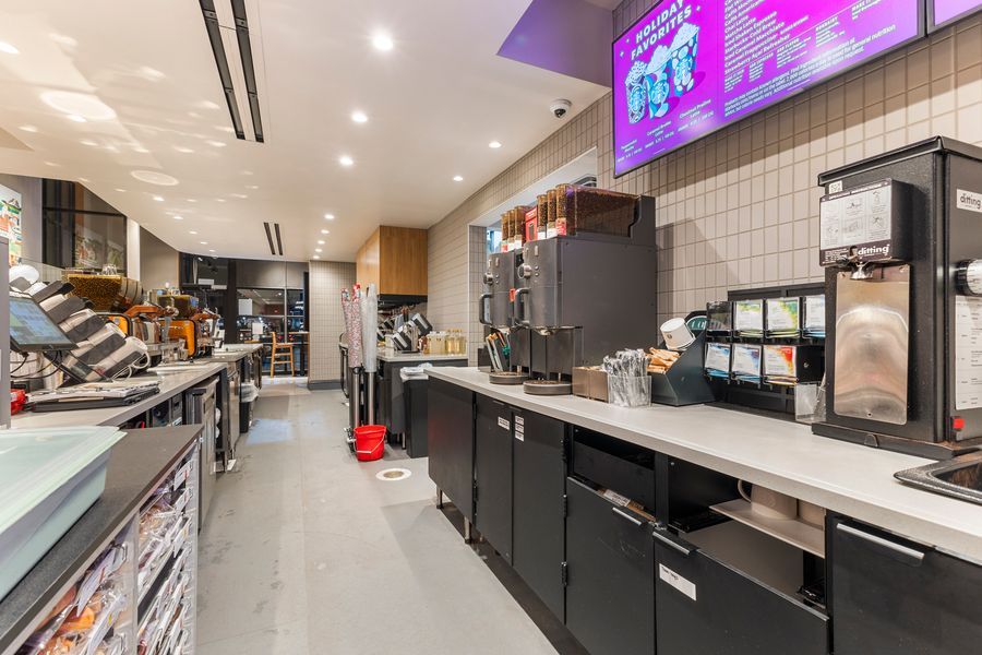 Modern fast food restaurant interior with black counters, coffee station, and digital menu board above.
