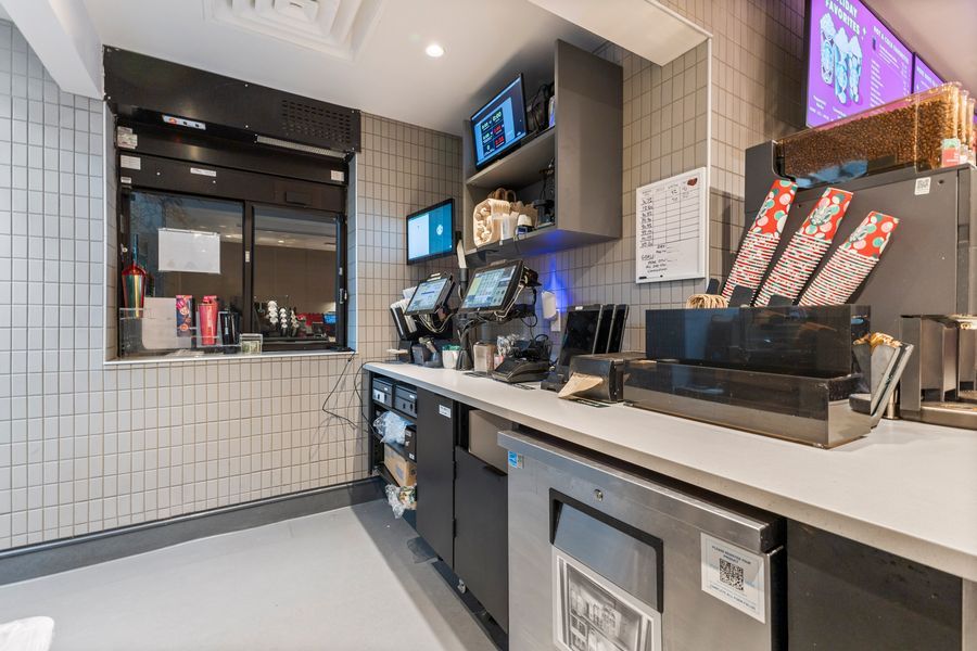 Modern fast food counter with self-serve beverage stations, POS terminals, and menu displays in a clean tiled interior.