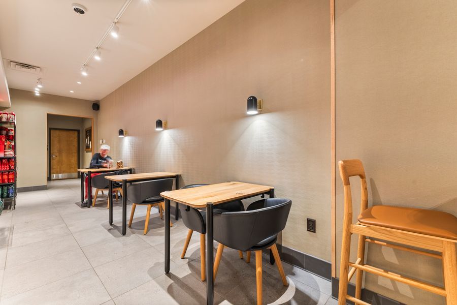 Modern cafe seating area with wooden tables, black chairs, and wall sconces in a minimalist interior.