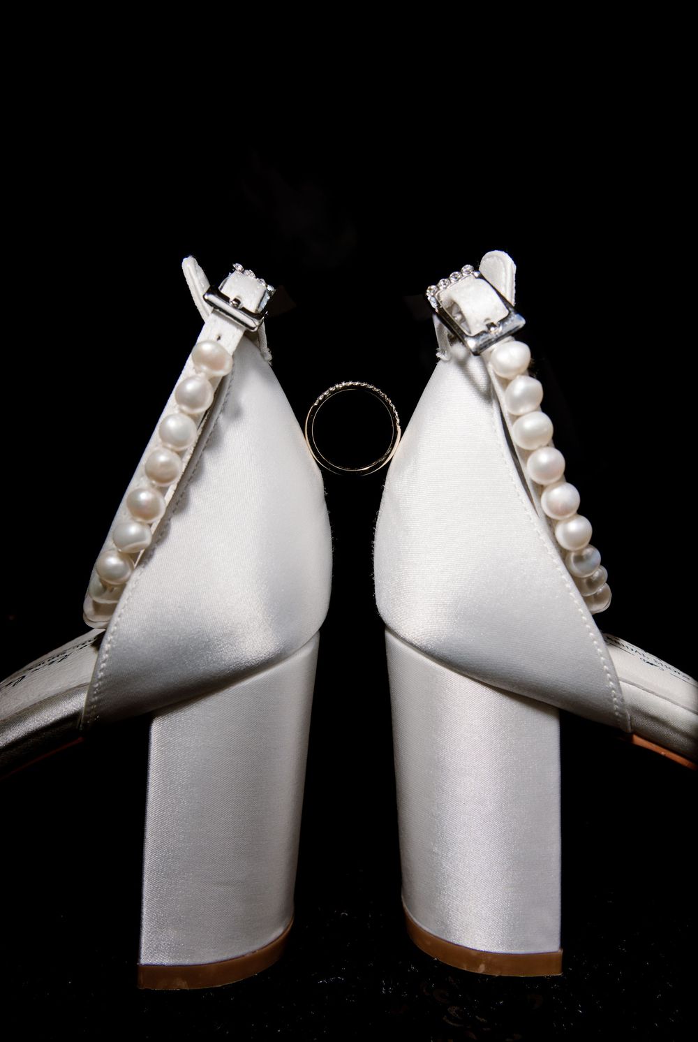 Back view of white satin pearl ankle-strap wedding heels with gold ring between them.
