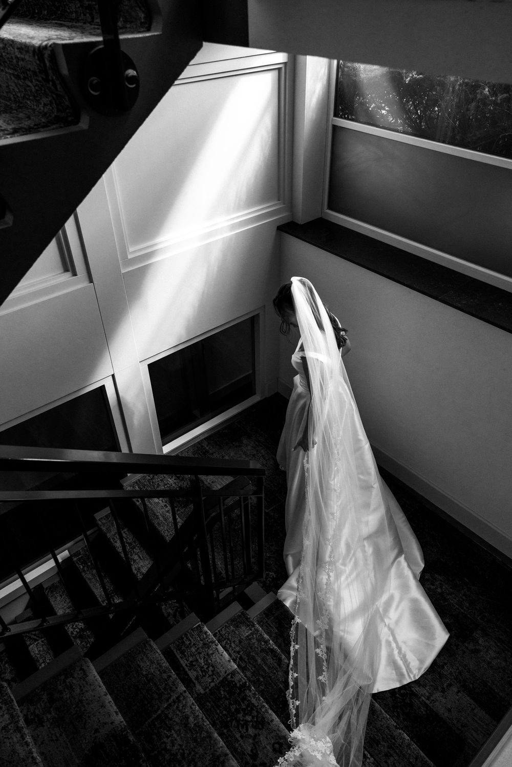 Bride in white gown and veil descending staircase in black and white wedding photography.