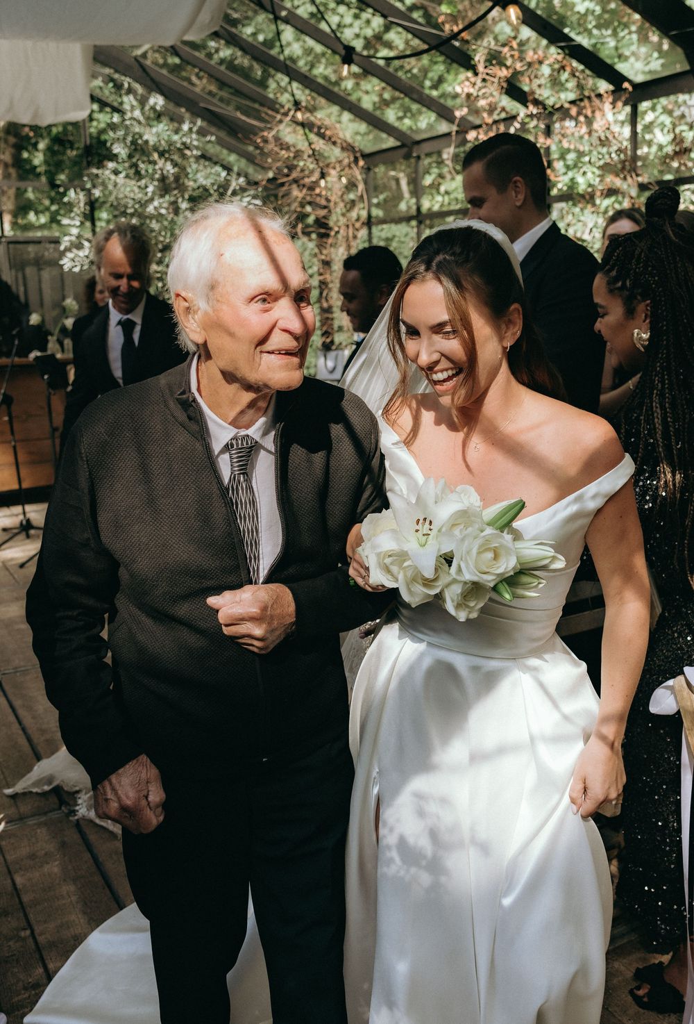 Elderly man walking bride down the aisle at outdoor wedding ceremony, bride holding white bouquet.