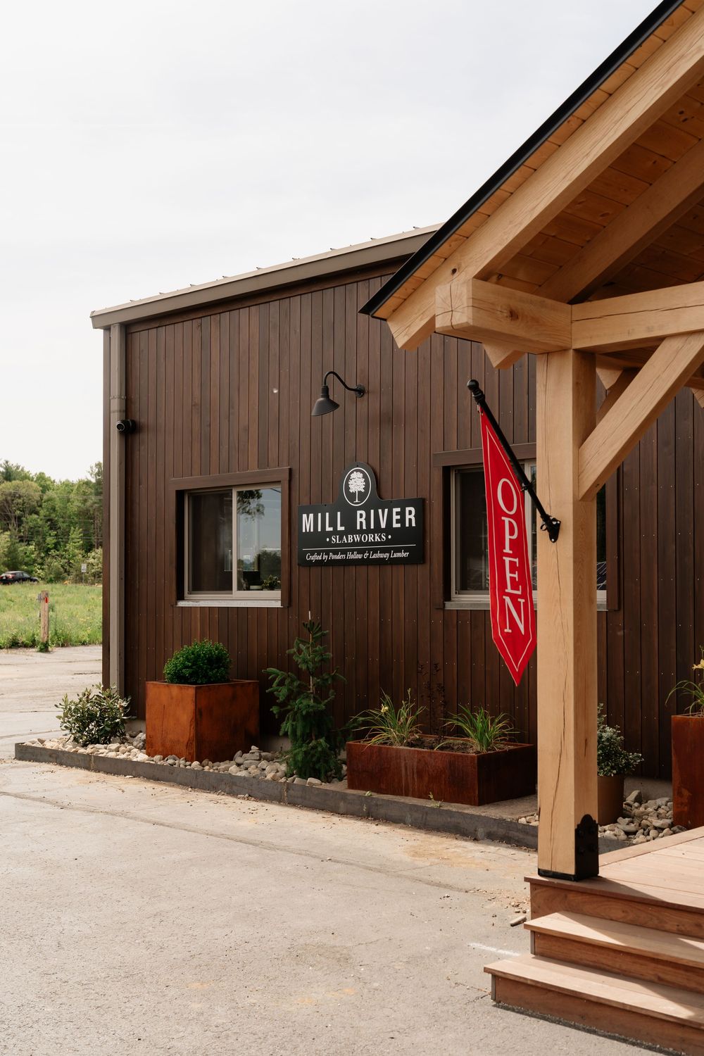 Exterior of Mill River Glassworks studio with dark wood siding, open sign, and timber frame entrance.