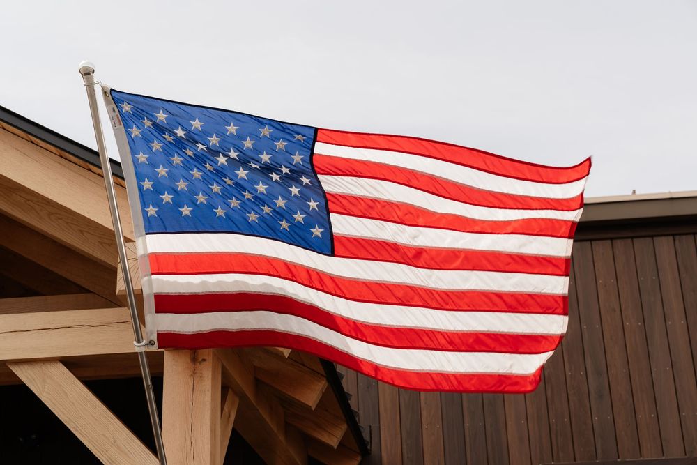 American flag waving proudly on a wooden building pole against a cloudy sky.