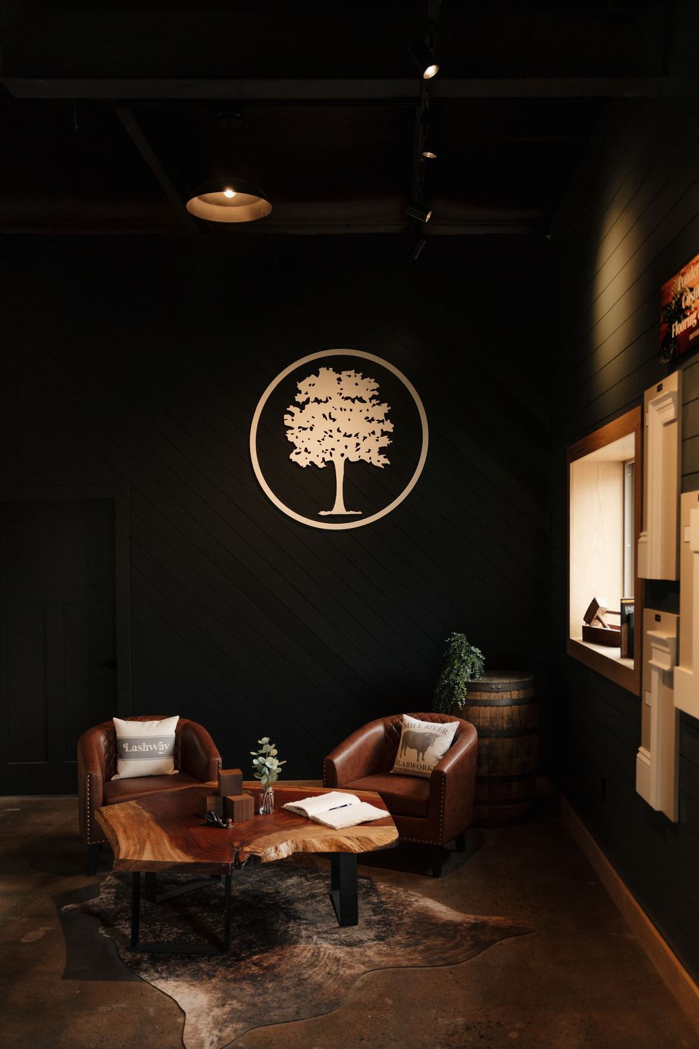 Cozy lounge with leather chairs, live-edge coffee table, and a tree logo on a dark wall.