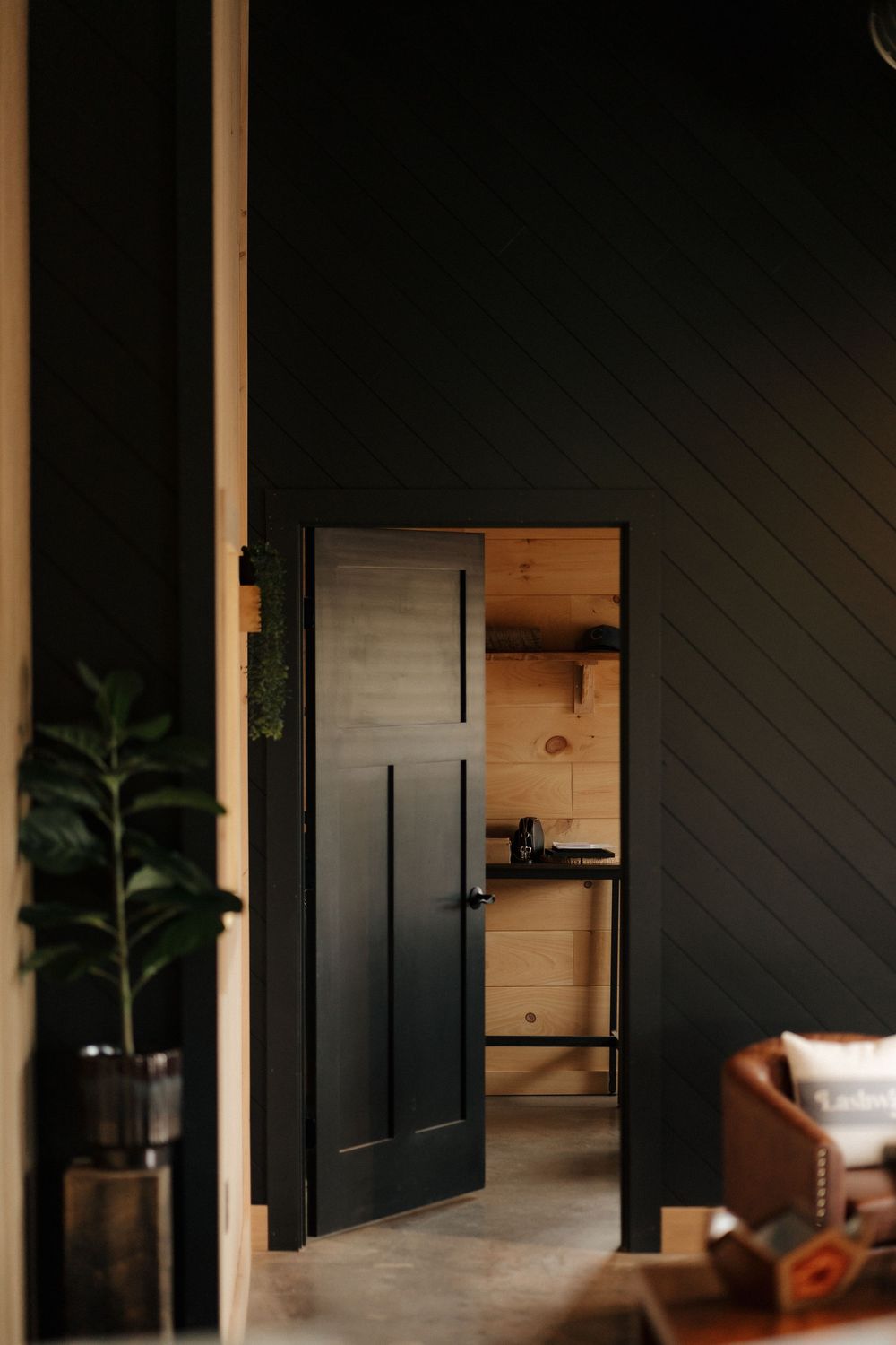 Dark black interior door open to a warm wood-paneled room with modern rustic decor and concrete floors.