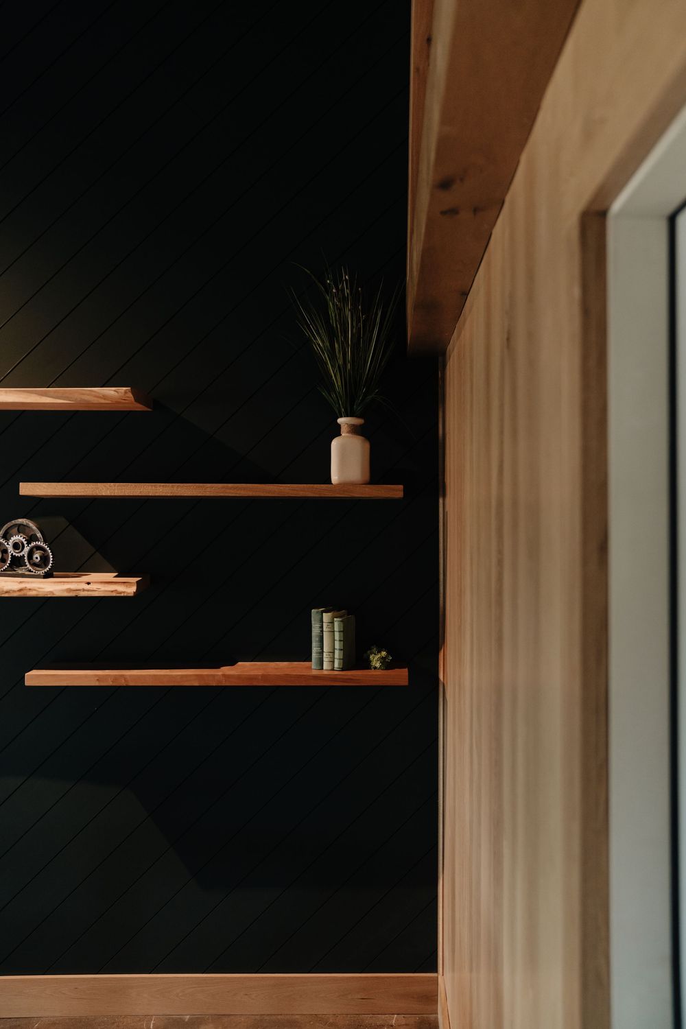Floating wood shelves on black shiplap wall displaying a vase with greenery and decorative books.