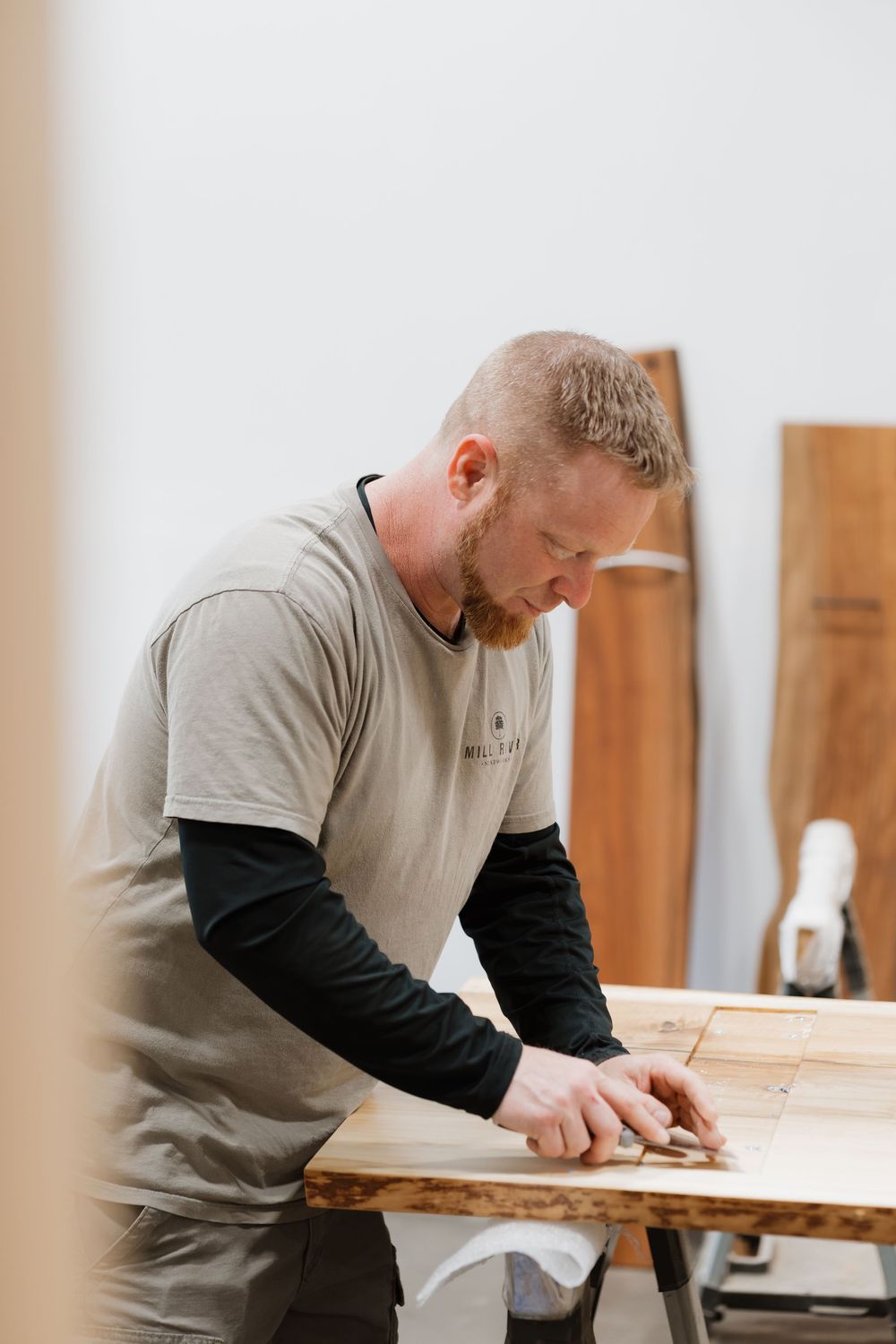 Craftsman measuring wood at a workbench in a bright woodworking studio workshop.