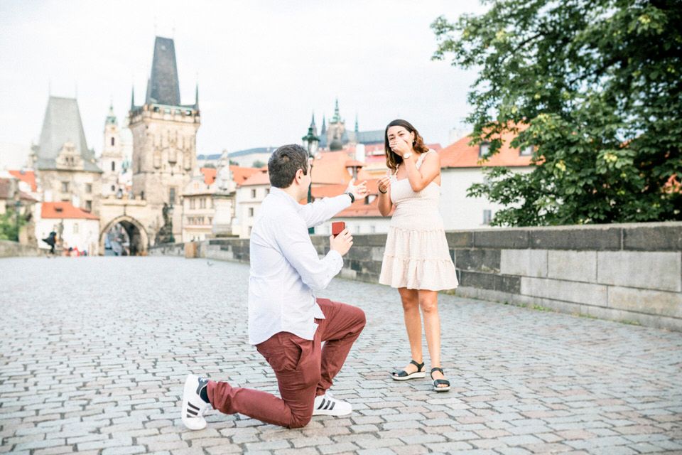 A romantic moment unfolds on the cobblestone Charles Bridge in Prague with historic architecture in background.