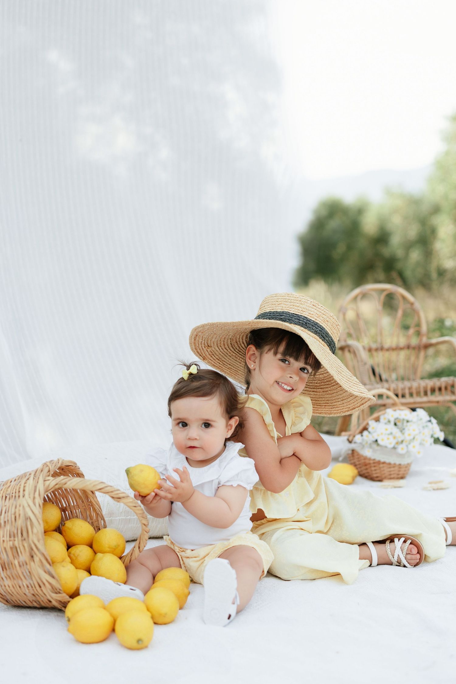 Young girl in straw hat and yellow sunglasses sitting in inflatable pool ring outdoors near a tree.