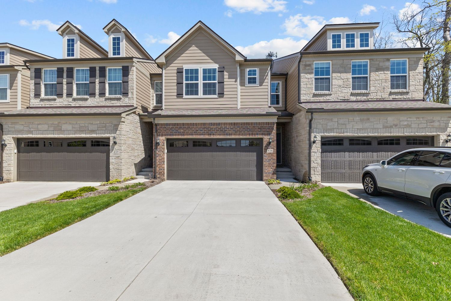 Modern townhome exterior featuring brick and stone facade, two-car garage, and concrete driveway.