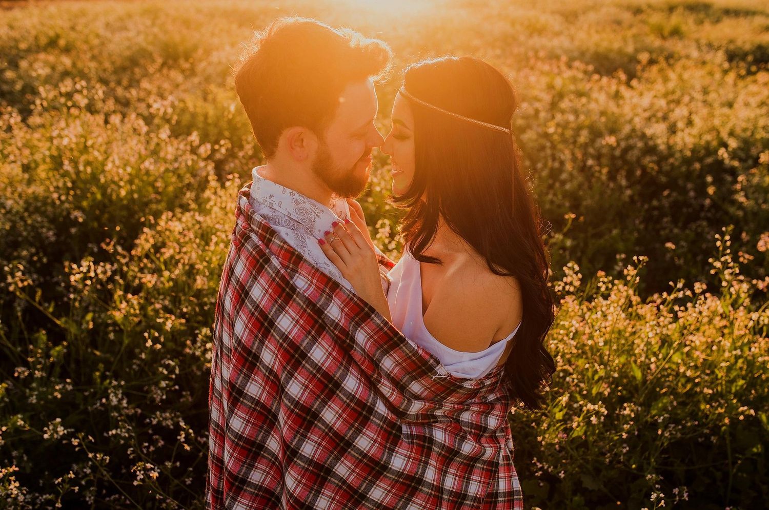 Un couple s'enlace dans un champ de fleurs baigné de soleil couchant, enveloppé dans une couverture à carreaux.