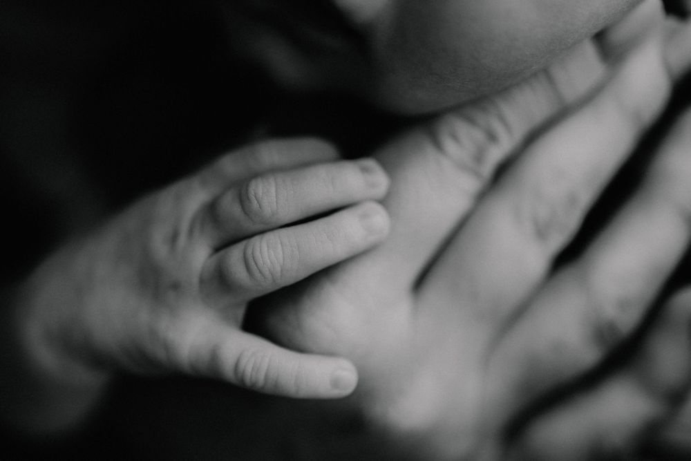 Black and white close-up of a newborn baby's tiny hand resting gently on an adult's chest.