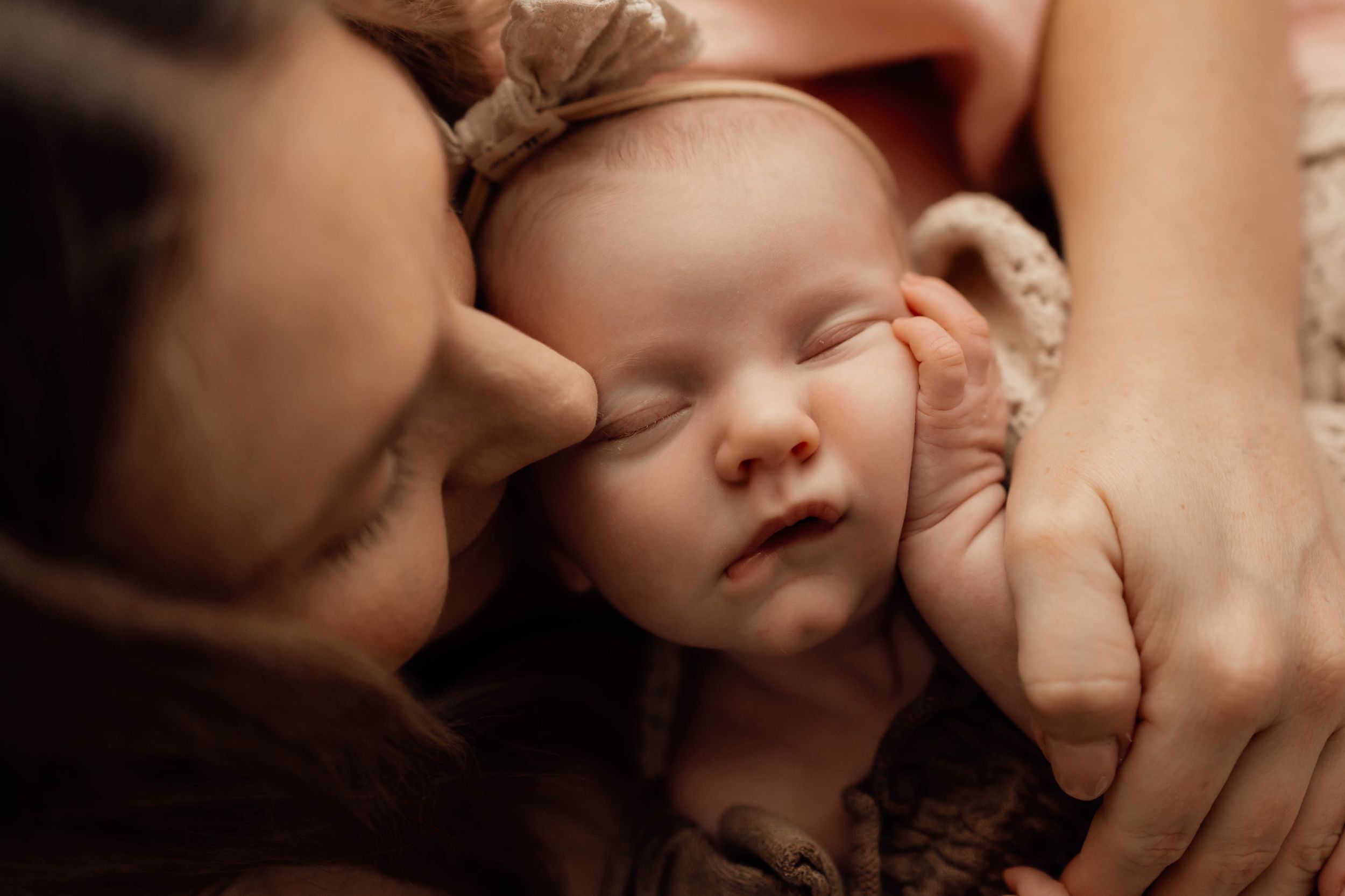 Close-up of a peaceful sleeping newborn baby with a bow headband being gently held by parents.