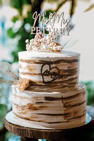 Two-tier rustic wedding cake with wood grain design, heart carving, and Mr & Mrs Pettrey topper on wooden stand.