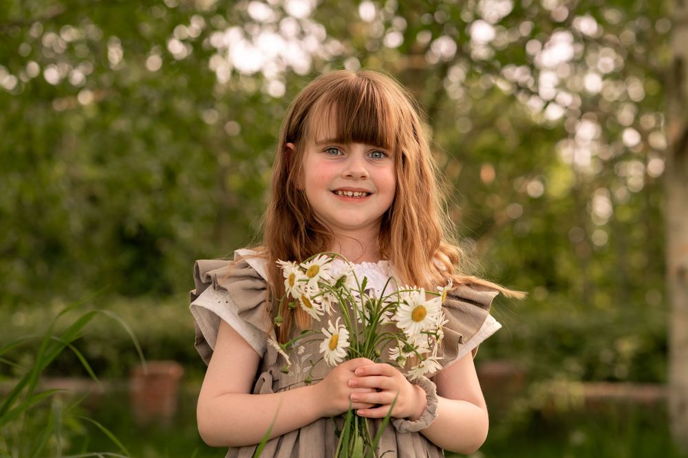 Young girl white daisy bouquet, smiling outdoors in lush green garden setting during childhood photoshoot in Lincolnshire.
