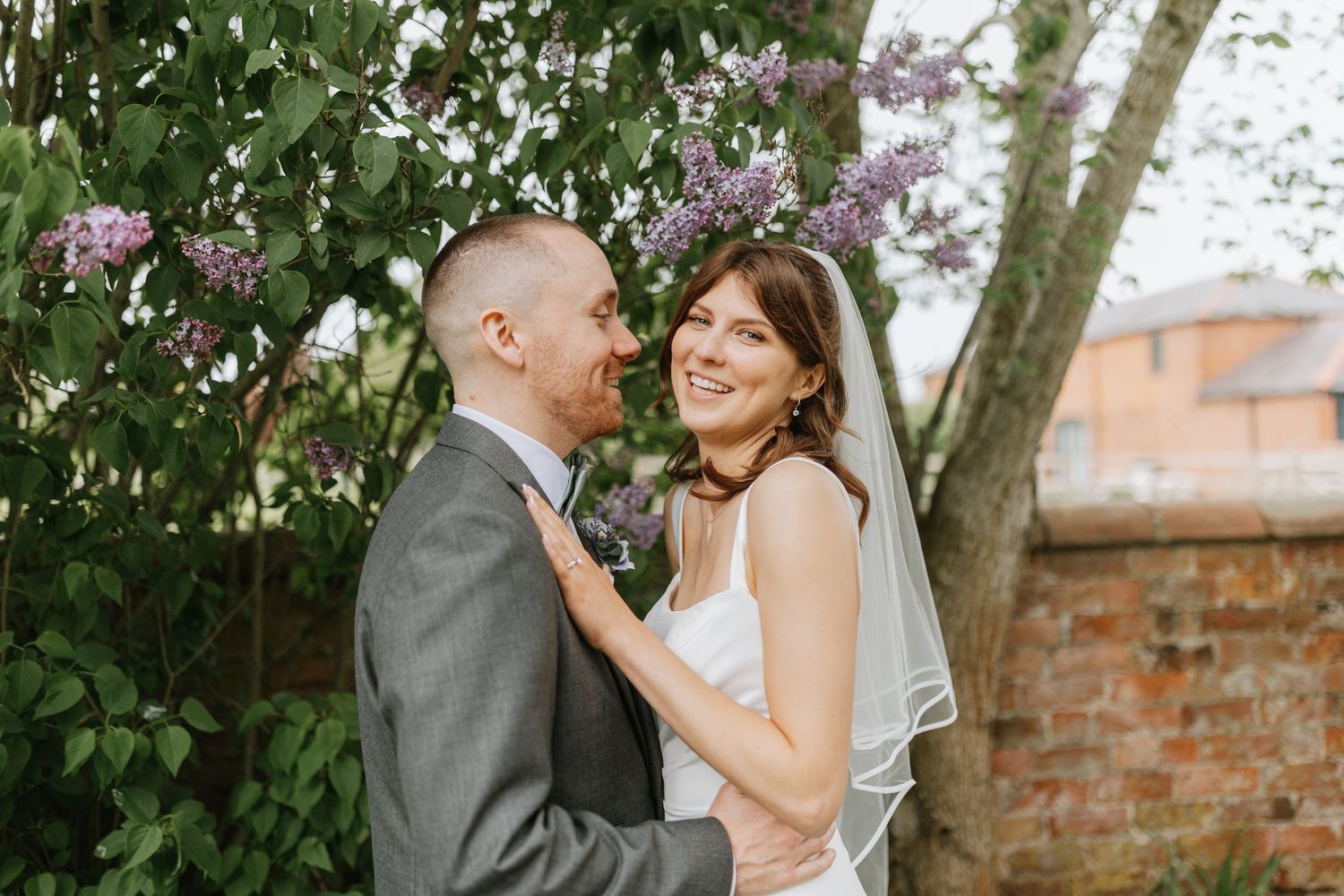 Black and white photo of a smiling bride in a veil and groom in a suit sitting together on a rope swing outdoors.