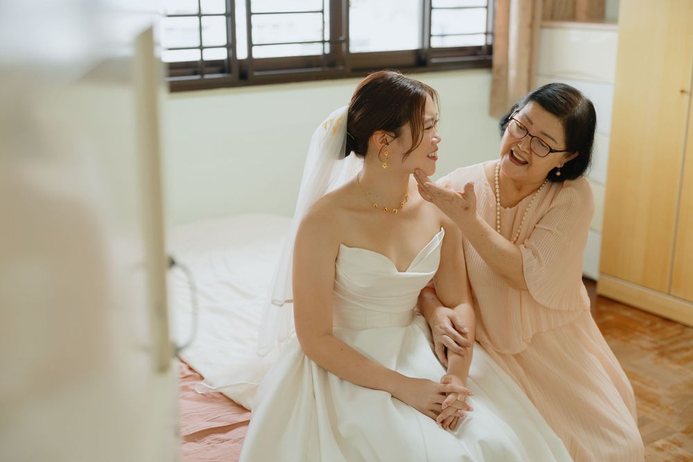 A bride in a white strapless gown and veil shares a joyful moment with an older woman in a pink dress.