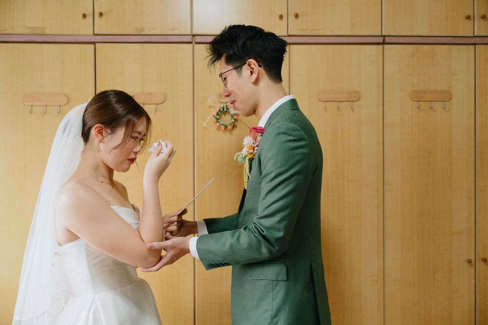 Bride and groom exchanging rings during wedding ceremony, groom in green suit with floral boutonniere.